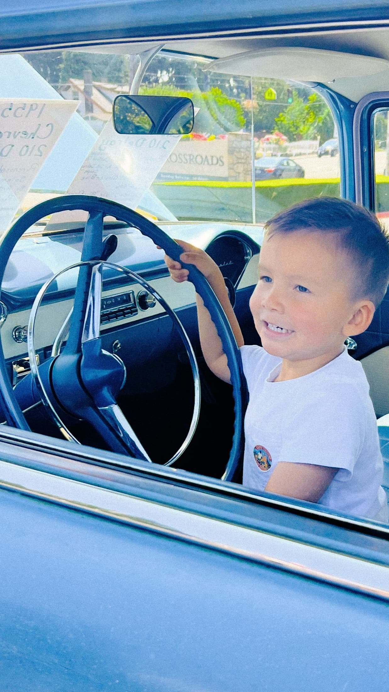 Child smiling from the window of a classic car.