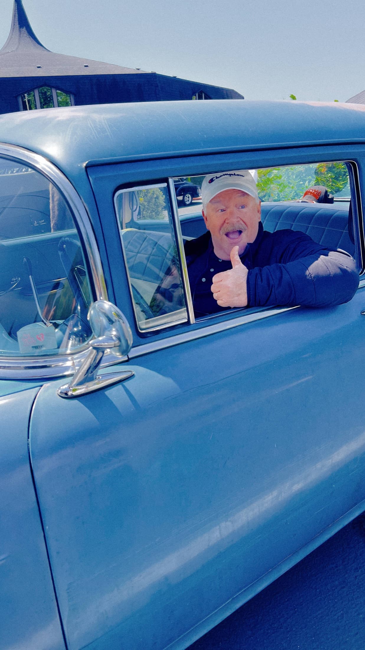 Guest smiling and giving a thumbs up from inside a classic car.